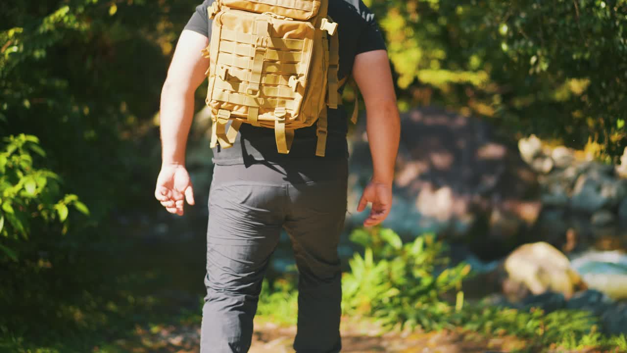 excursionista masculino que atraviesa un río de montaña rodeado de rocas y árboles