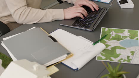 camera focuses on the hands of man typing on keyboard laptop sitting at desk in the office