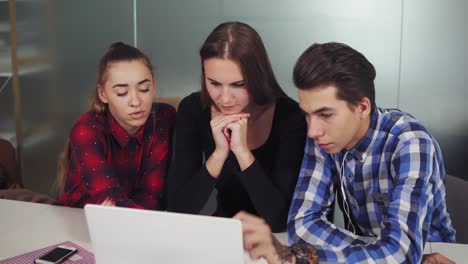 un grupo de jóvenes trabajadores creativos en un entorno de trabajo de creación que celebran una reunión de proyecto en torno a una computadora en una sala de conferencias. señalan a la pantalla y discuten el proyecto