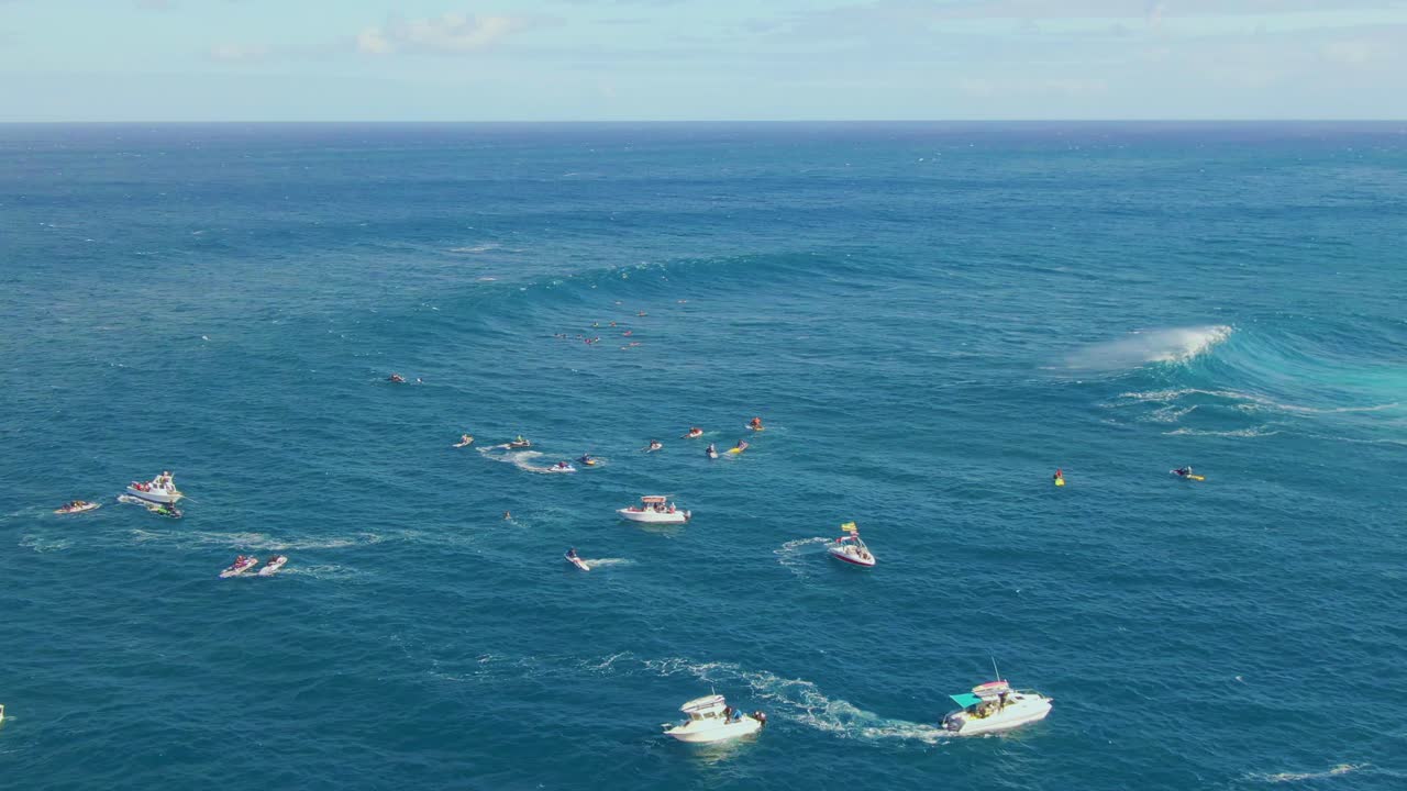 Surfers and rescue boats swim on dangerous waters of deep blue ocean with big white waves in Hawaii