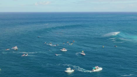 Surfers and rescue boats swim on dangerous waters of deep blue ocean with big white waves in Hawaii