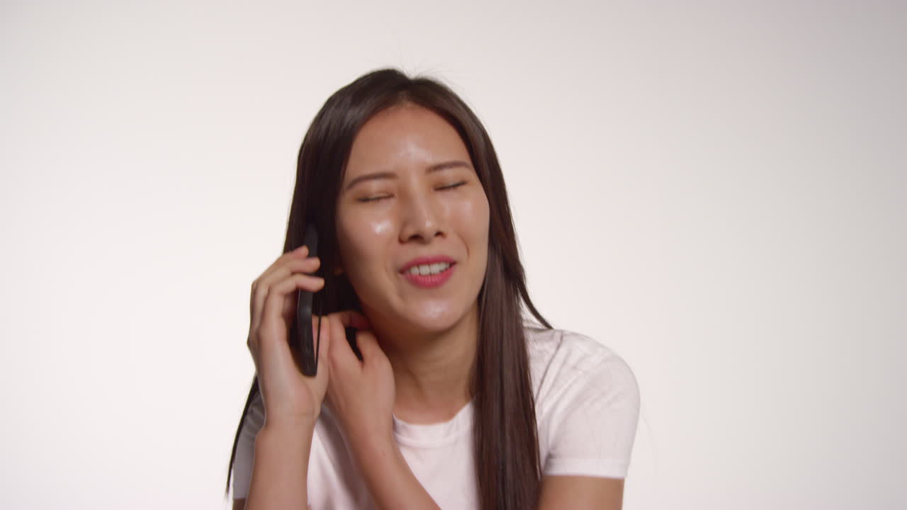 색 스튜디오 배경 앞에 휴대전화를 들고 있는 젊은 여성이 사진 부스 스타일의 초상화를 위해 포즈를 취하고 있다.