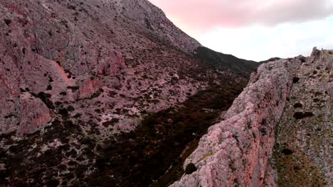 scenic view at the red rocky cliff of mountain partly covered in green plants in greece. - aerial drone shot