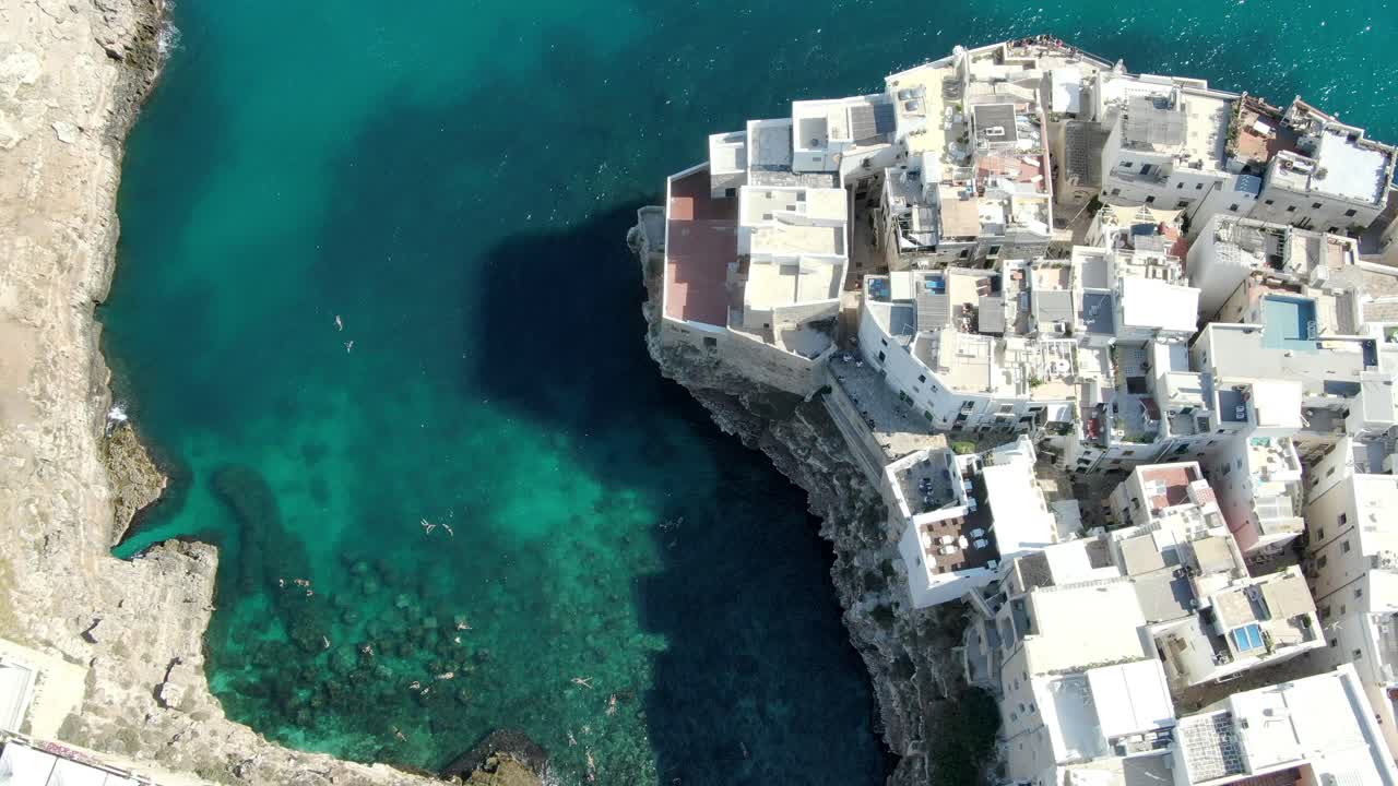 drone captura tiro de gran altitud de polignano a mare una ciudad en italia con numerosos edificios construidos en el borde del acantilado con gente nadando en el mar adriático