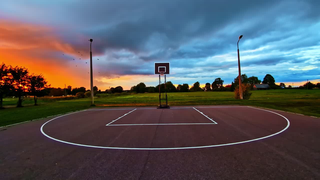 Empty basketball court under dramatic sunset sky with vivid orange and blue colors