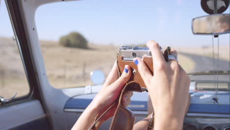 hermosa chica tomando fotos con una cámara vintage en un viaje por carretera en un coche convertible