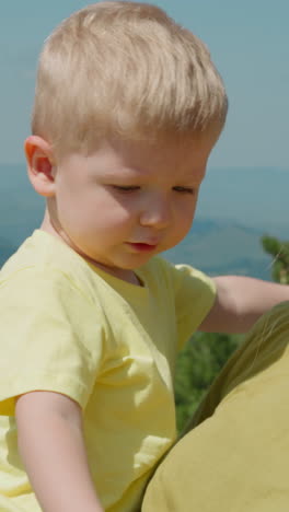 pretty mother with long loose hair cuddles chubby cheeks little son against old distant mountains in mist at resort closeup slow motion