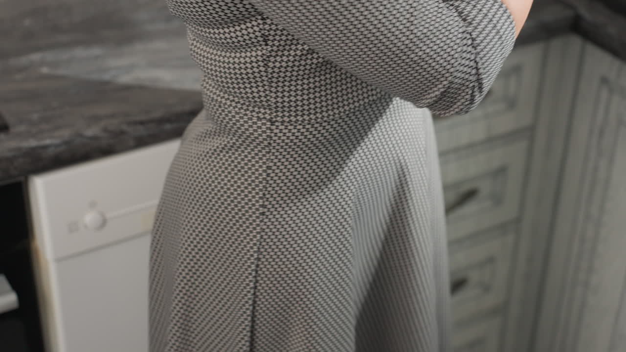 Lower body view of woman in plaid patterned gown standing close to kitchen cabinet, focused and busy with task, bright modern kitchen background