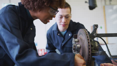 tutor with female students checking car brake discs on auto mechanic course at college