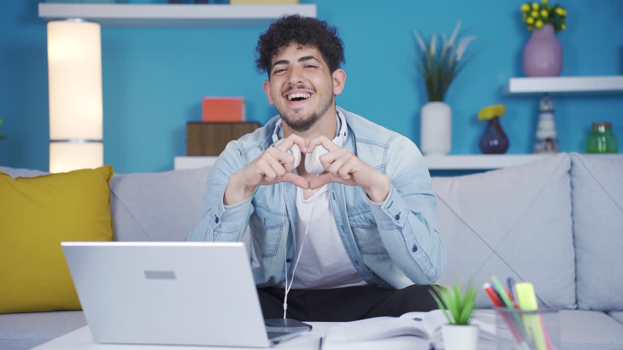 학생은 카메라를 위해 심장을 만 ⁇ 니다. 그는 미소 짓고 카메라를 쳐다본다.