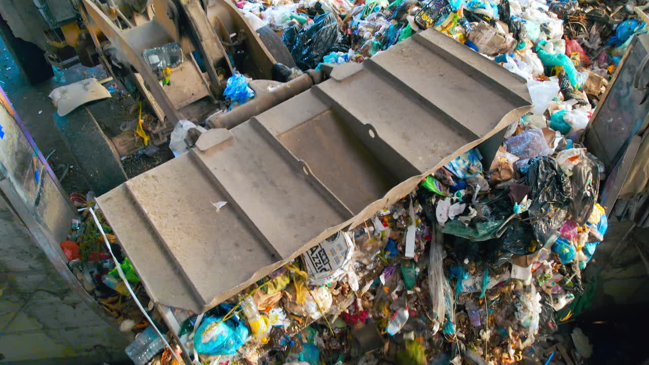 An excavator loading garbage onto a conveyor belt at waste sorting plant. Slow motion