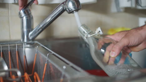 imágenes de un hombre llenando una botella de vidrio con agua del grifo de la casa