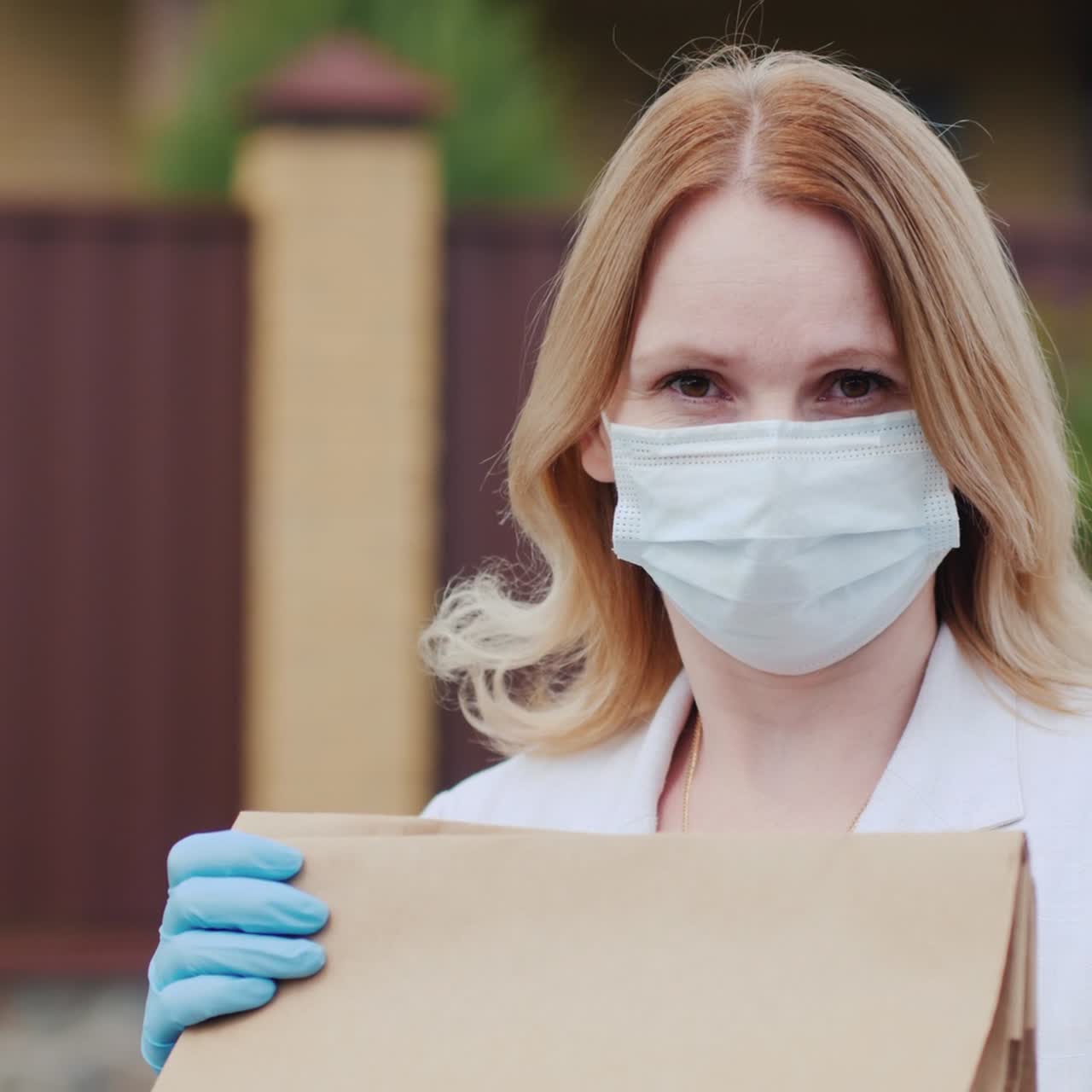 식료품 가방을 들고 있는 마스크 쓴 여성의 초상화가 그녀의 집 근처에 서 있다