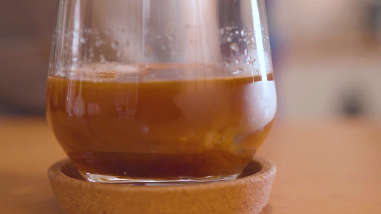 Versamento di caffè espresso su cubetti di ghiaccio fusi in un bicchiere.
