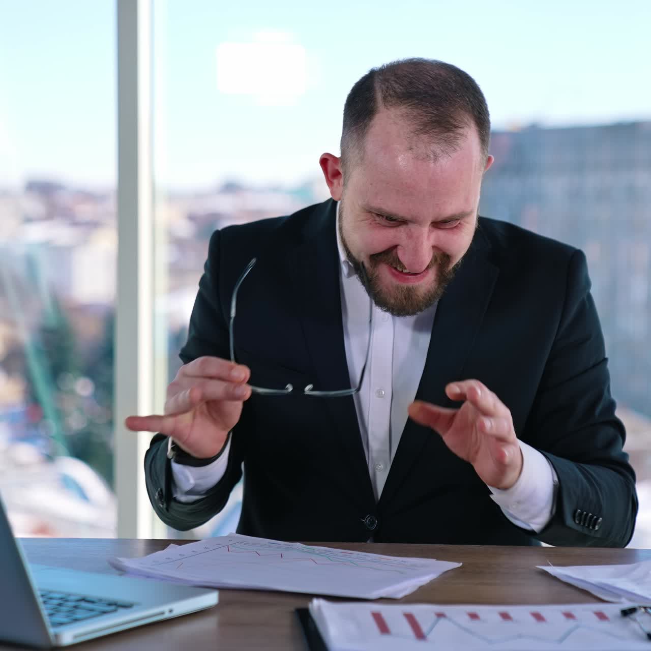 Empresário engraçado. Homem insano de terno sentado à mesa no centro do escritório e fazendo coisas loucas com os braços e dedos.