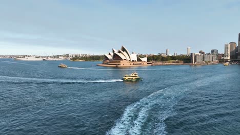 Impresionante-Toma-Aérea-De-Aproximación-De-La-Emblemática-ópera-Australiana-De-Sydney-Con-Ferries-De-Pasajeros-Debajo,-Australia