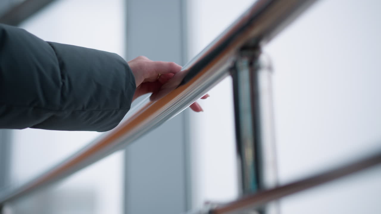 큰 유리 창문이 있는 현대적인 건물에서 는 동안 매끄러운 철도에서 미끄러지는 반지로 장식된 여성 손의 클로즈업