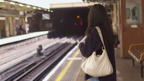 young woman with mobile phone waiting for train on underground railway station platform