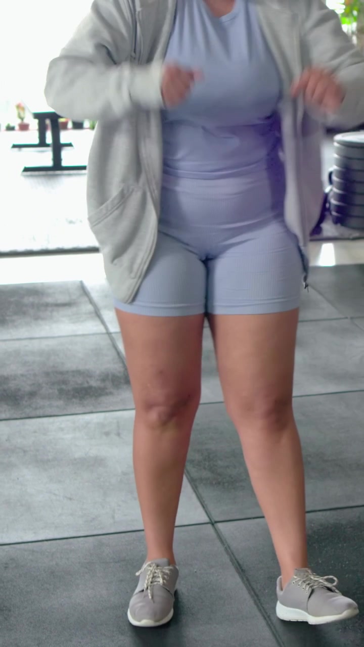 Video verticale: Una donna in viola allaccia la scarpa, lega i lacci in palestra e indossa le cuffie per l'allenamento