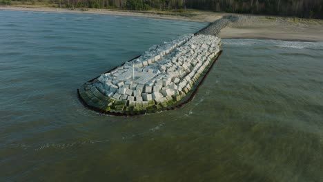 vista aérea del muelle protector con bloques de hormigón y rocas en la costa del mar báltico en liepaja, letonia, fortaleciendo la playa contra la erosión costera, disparo de drones que avanza inclinado hacia abajo