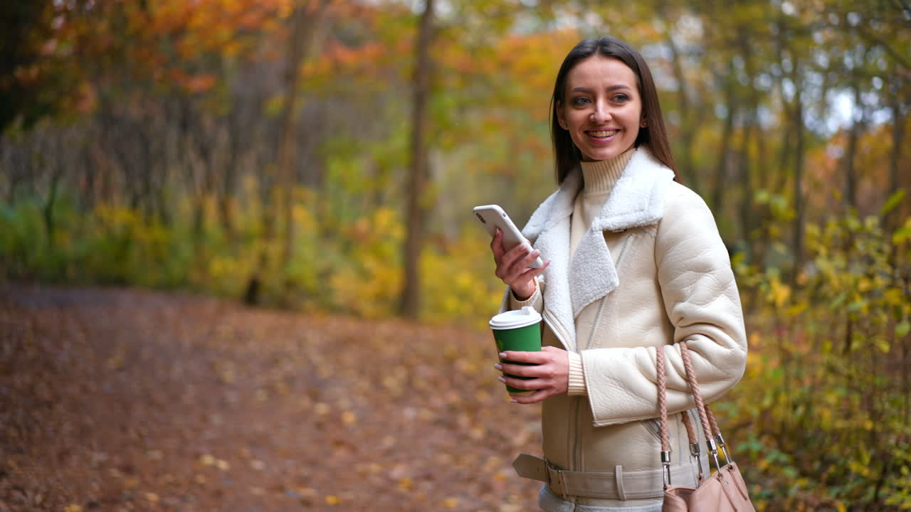 Woman enjoying coffee and phone in an autumn park