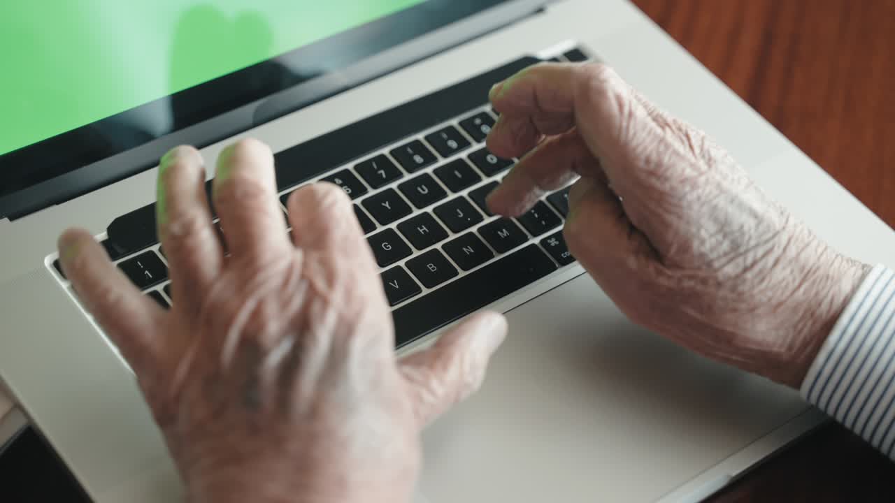 vista superior de un jubilado con las manos arrugadas escribiendo en un teclado de computadora de moda con pantalla verde, un anciano trabajando en casa usando una computadora portátil moderna y aplicaciones en línea. manos de un anciano escribiendo