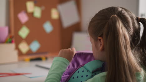 Little-schoolgirl-puts-textbook-from-schoolbag-on-desk