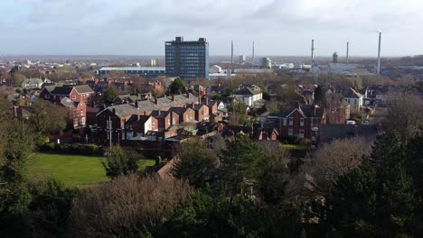 Aerial-view-over-park-trees-to-industrial-townscape-buildings-with-blue-skyscraper,-Merseyside,-England