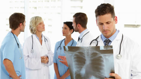 Serious-doctor-holding-xray-while-staff-are-standing-behind-him