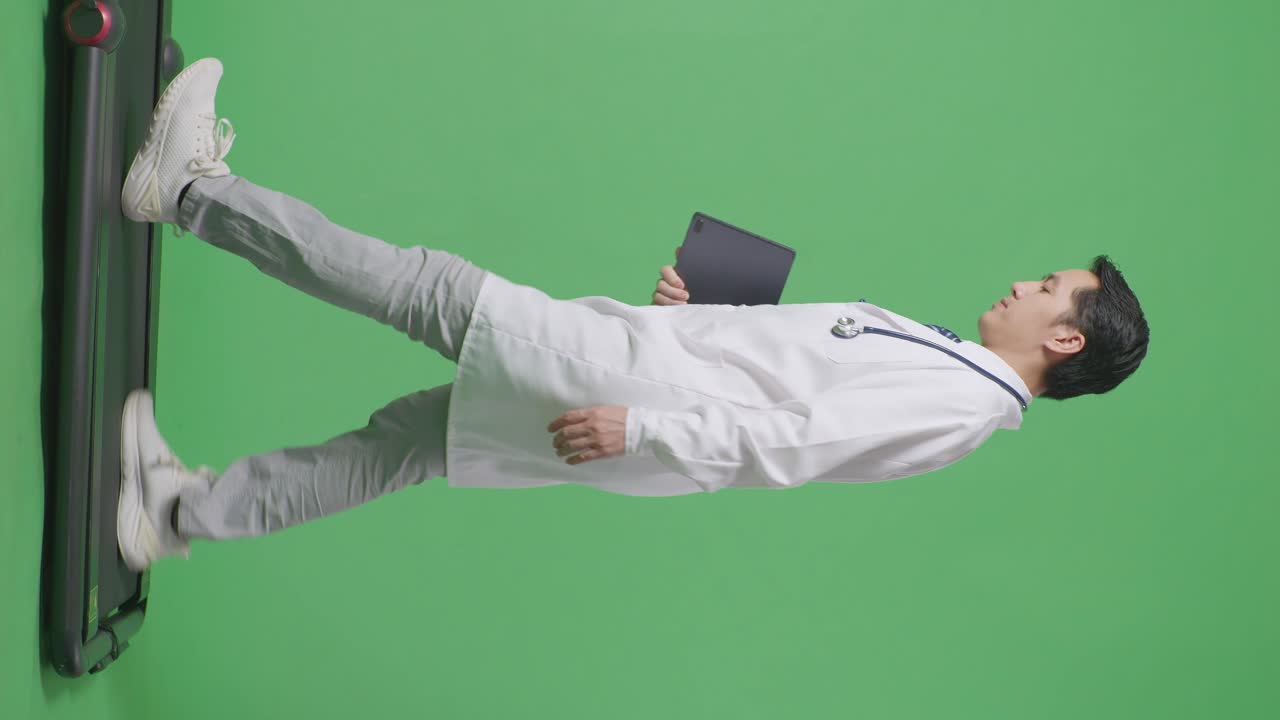 아시안 남성 의사가 스테토스코프를 들고 병원에서 녹색 화면 배경에서 는 동안 태블릿을 들고 있습니다.