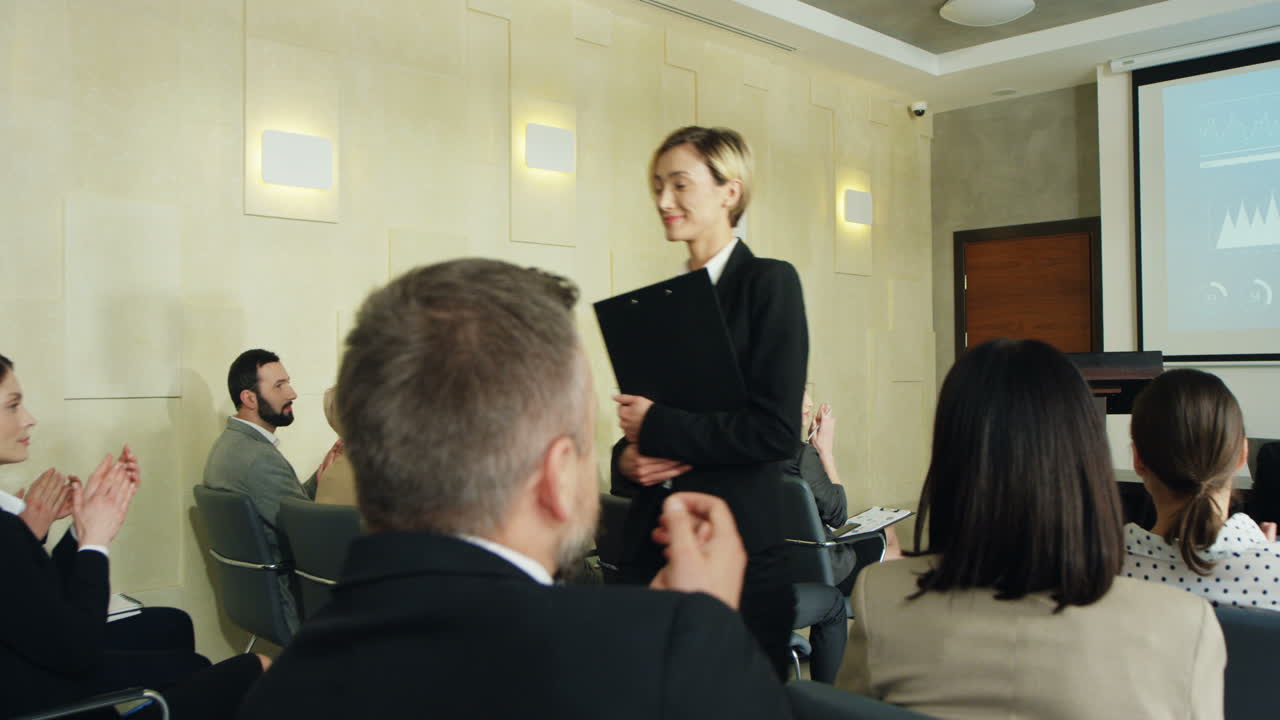 Caucasian female business speaker finishing her conference in a meeting and going away cheerfully while people clapping