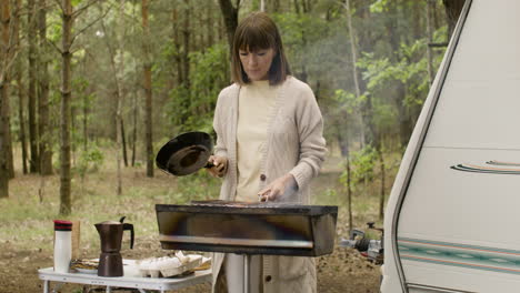 mujer cocinando en la barbacoa en el camping en el bosque