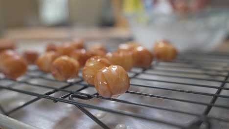 woman places fresh donut holes dripping in glaze on cooling rack, close up