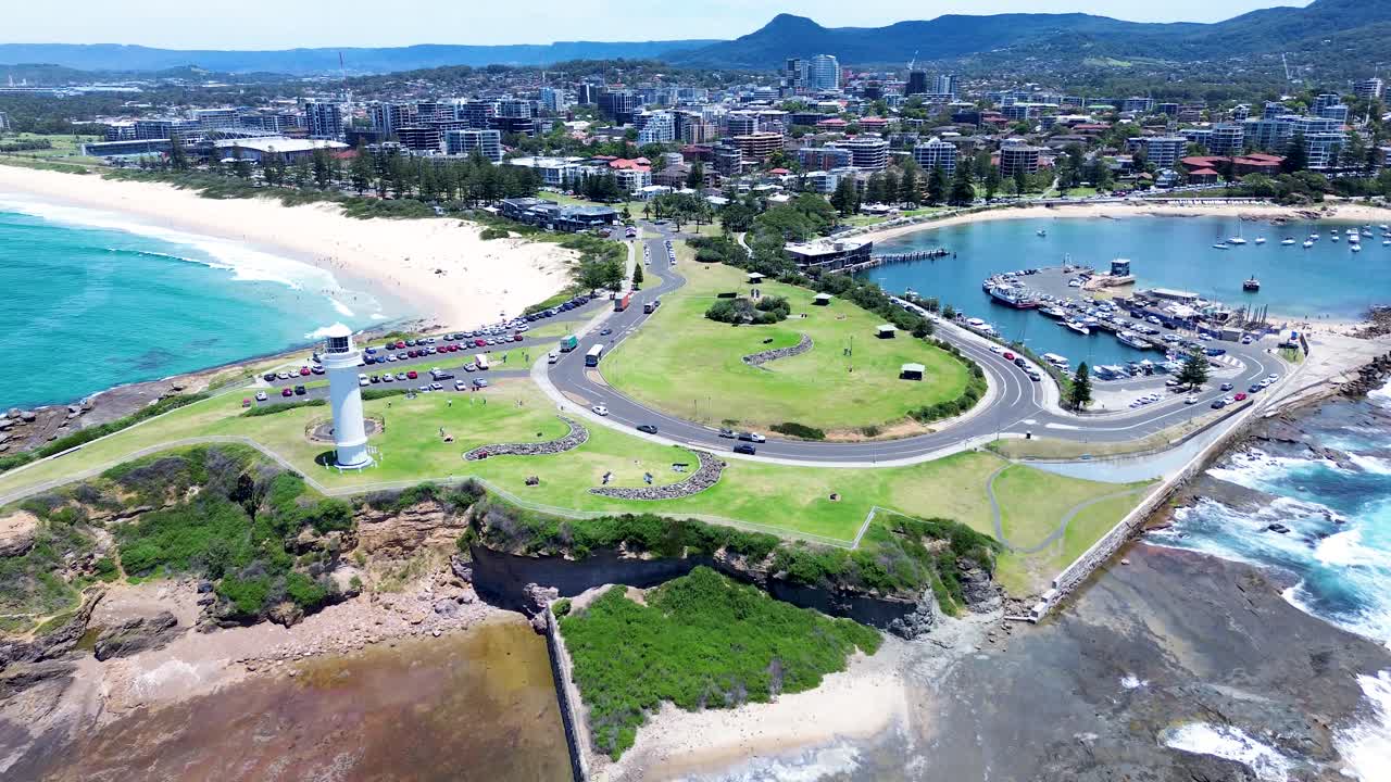 Drone aerial landscape of ocean waves crashing along coastline headland at Flagstaff Point Lighthouse with car driving past main road Wollongong Beach in Illawarra South Coast Australia travel tourism