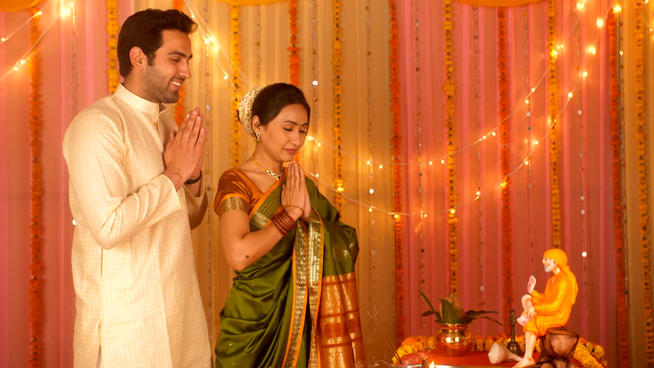 Indian married couple wearing ethnic clothes for Puja at home - Offering prayers to Sai Baba