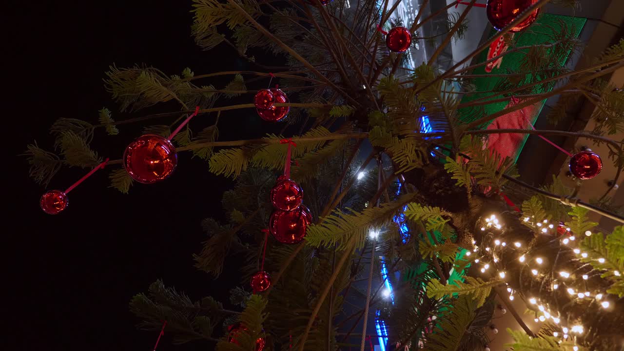 decoraciones de navidad brillantes y luces brillantes que adornan un árbol de navidad colocado frente a un edificio ubicado en una ciudad del sudeste asiático
