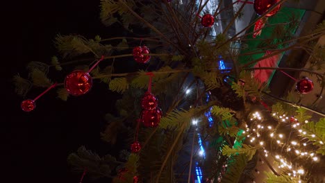 shiny christmas decors and bright lights adorning a christmas tree placed in front of a building located in a southeast asian city