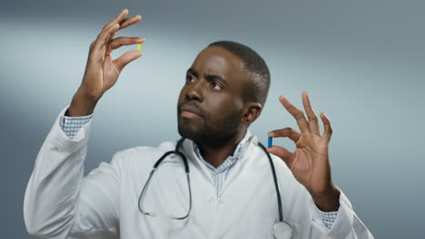 Young-Male-Physician-Holding-Two-Pills-In-Hands,-One-Yellow-And-One-Blue,-While-Comparing-Them-And-Studying-Carefully