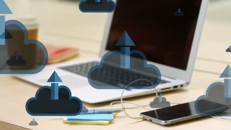 Animation-of-clouds-and-arrows-icons-over-smartphone-and-laptop-on-desk
