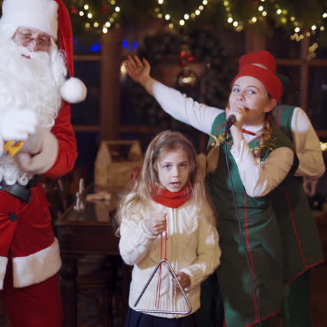 christmas celebration with santa. fairy elves, santa and children are singing and dancing on christmas background indoors.