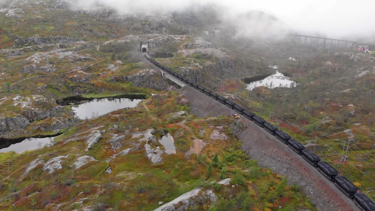 aéreo: tren de mineral en la estación de søsterbekk, cerca de la frontera entre suecia y noruega en el norte de laplandia entrando en un túnel