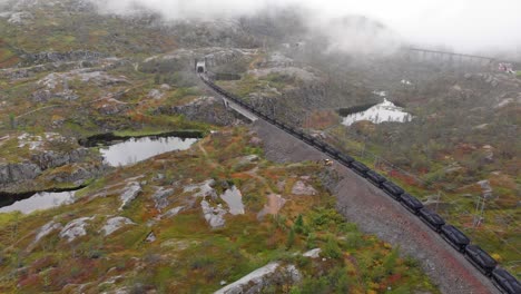 Aerial:-ore-train-in-Søsterbekk-stasjon,-close-to-the-border-between-Sweden-and-Norway-in-north-Lapland-entering-a-tunnel