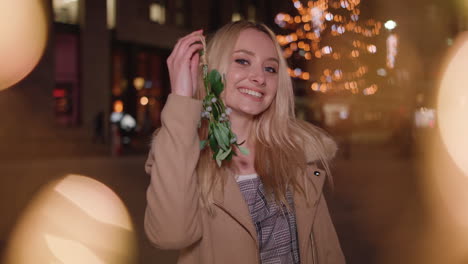 young lady waves mistletoe in the air and smiles at you - in slow motion