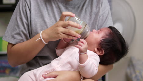 crying as it is waiting to be fed, a newborn child feeds on a formula milk in a feeding bottle held by her mother