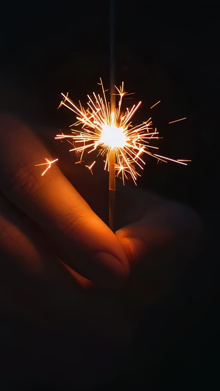Vertical video: Holding sparkler with single hand, lighter igniting core, sparks radiating at night
