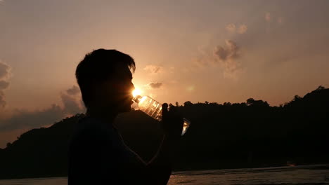 man drinking water at sunset by river