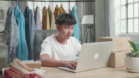 asian man online seller typing on computer while selling clothes at home
