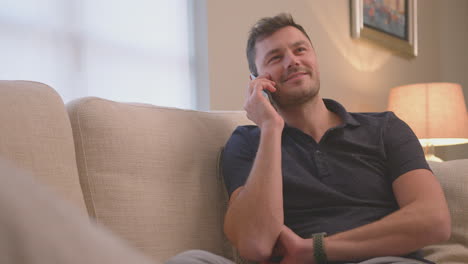 Evening-shot-of-man-relaxing-on-sofa-at-home-talking-on-mobile-phone---shot-in-slow-motion