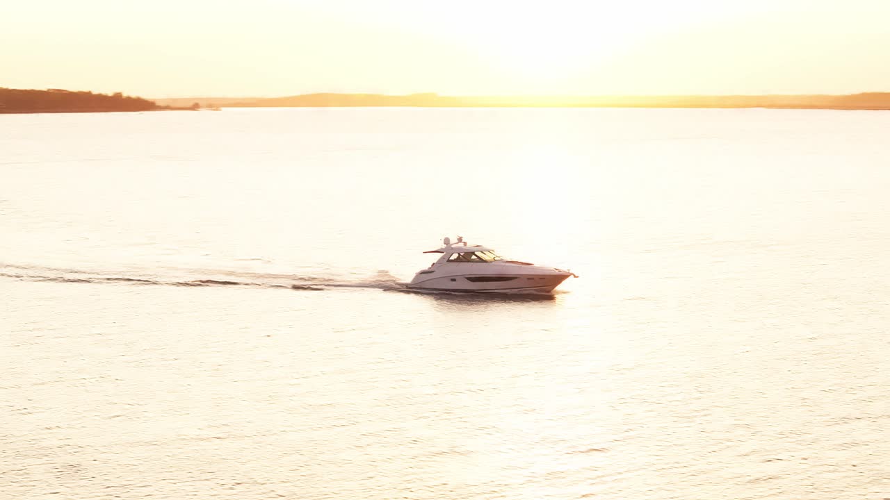 Silhouette of yacht boat approaching to pier as sun sets over South Carolina harbor skyline, aerial tracking backlit orbit