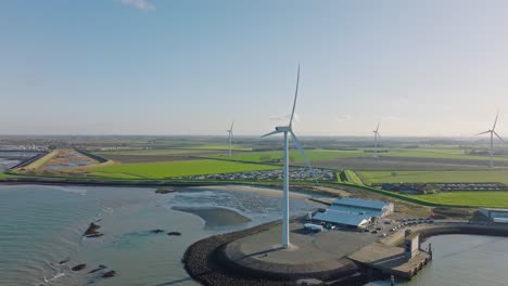 aerial slow motion shot of wind turbines in a rural, coastal area in the netherlands against a blue sky around sunset